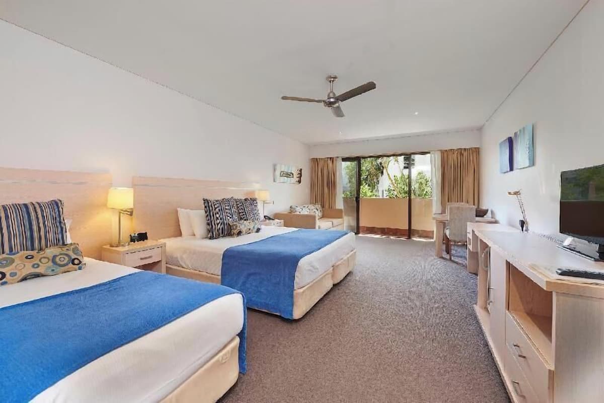 A hotel room with two beds, a desk, a television, and a ceiling fan.