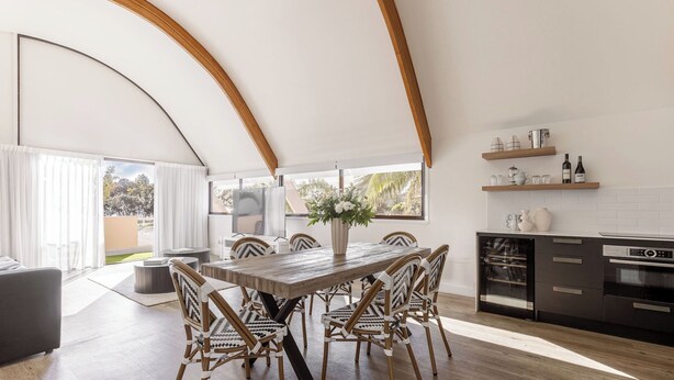 A modern kitchen with a dining area, wooden beams, and a large window. - Waves Byron Bay (Byron Bay)