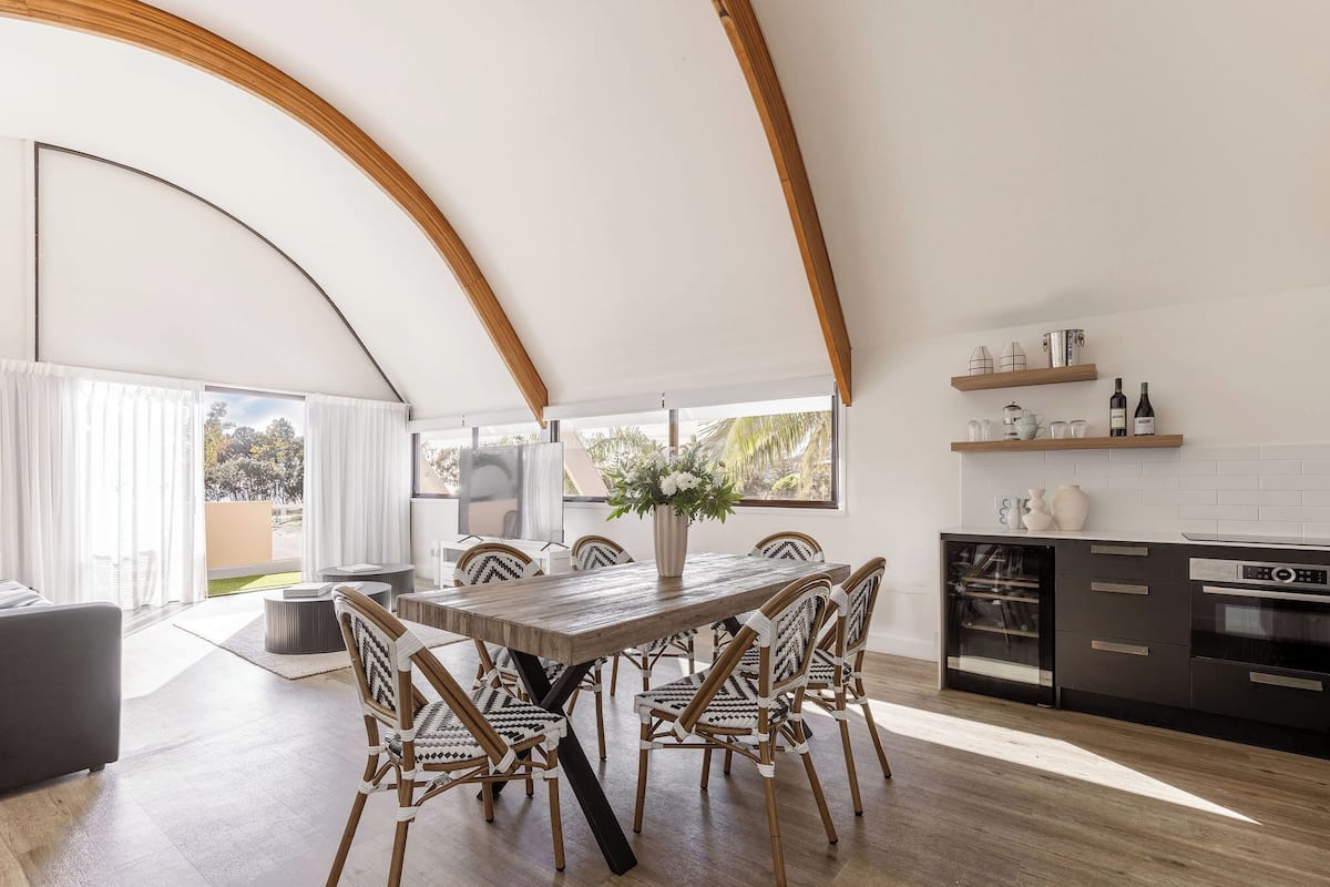 A modern kitchen with a dining area, wooden beams, and a large window.