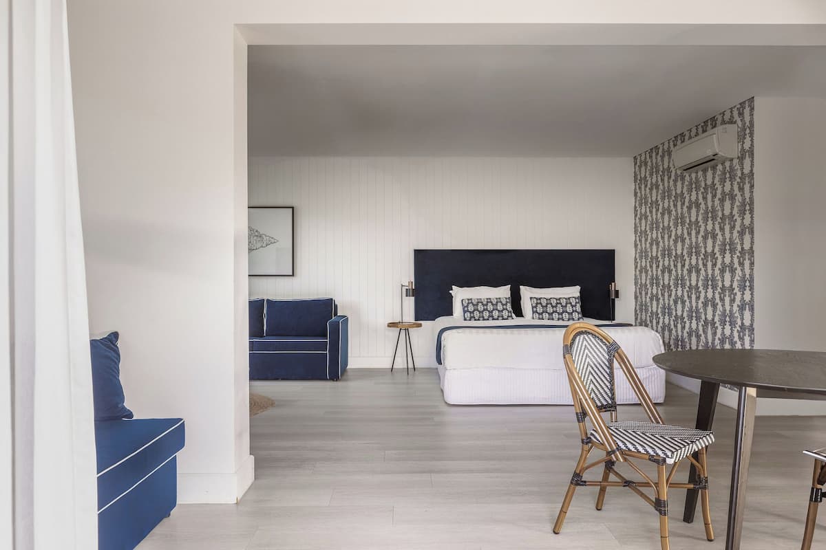 A modern hotel room with a bed, a blue sofa, a dining table, and a chair.