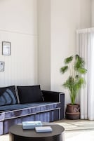 Una sala moderna con un sofá azul oscuro, una mesa de centro redonda y una planta grande en maceta.