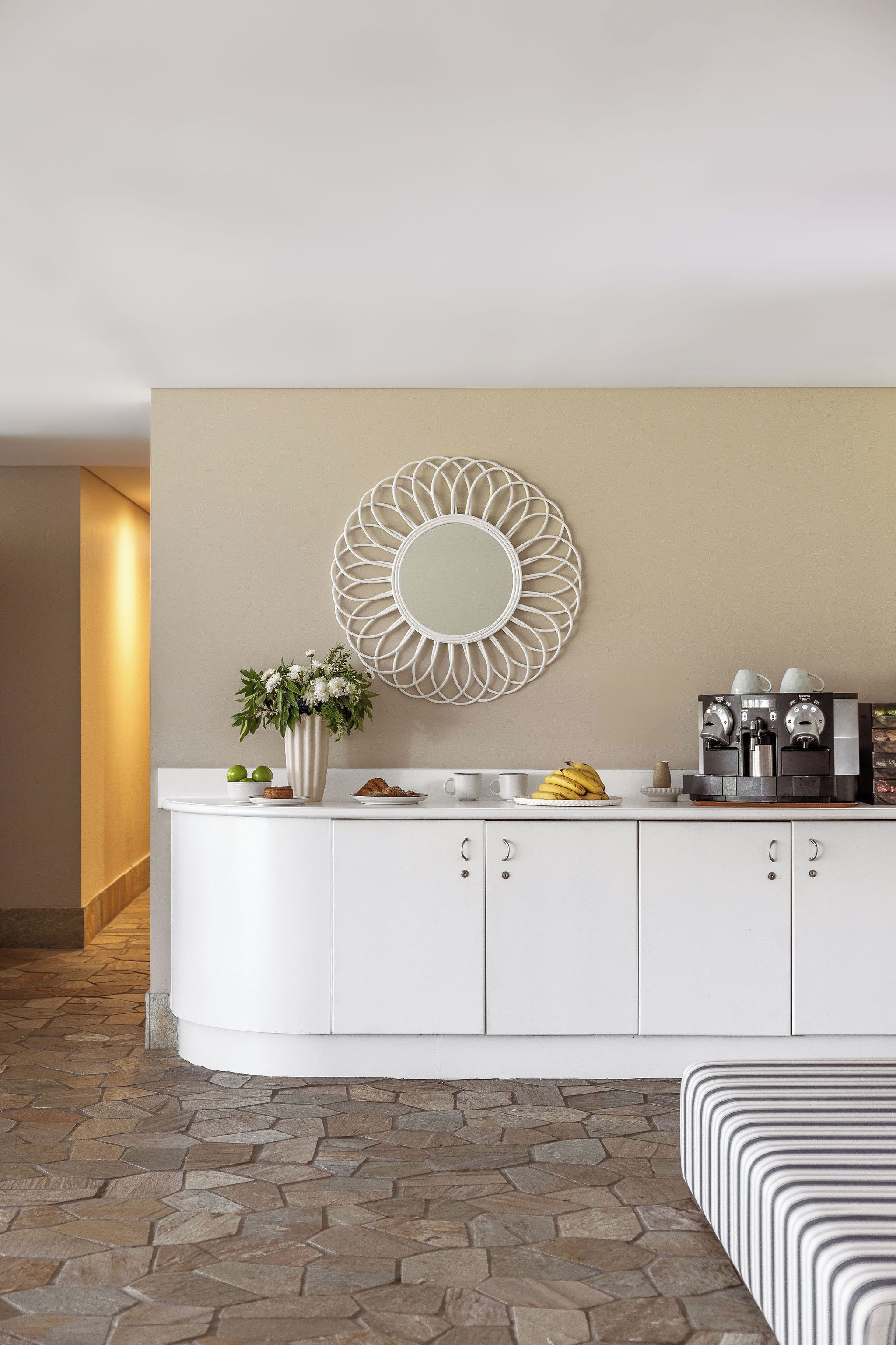 Une cuisine moderne avec un plan de travail blanc, un miroir décoratif, une machine à café et une plante en pot.