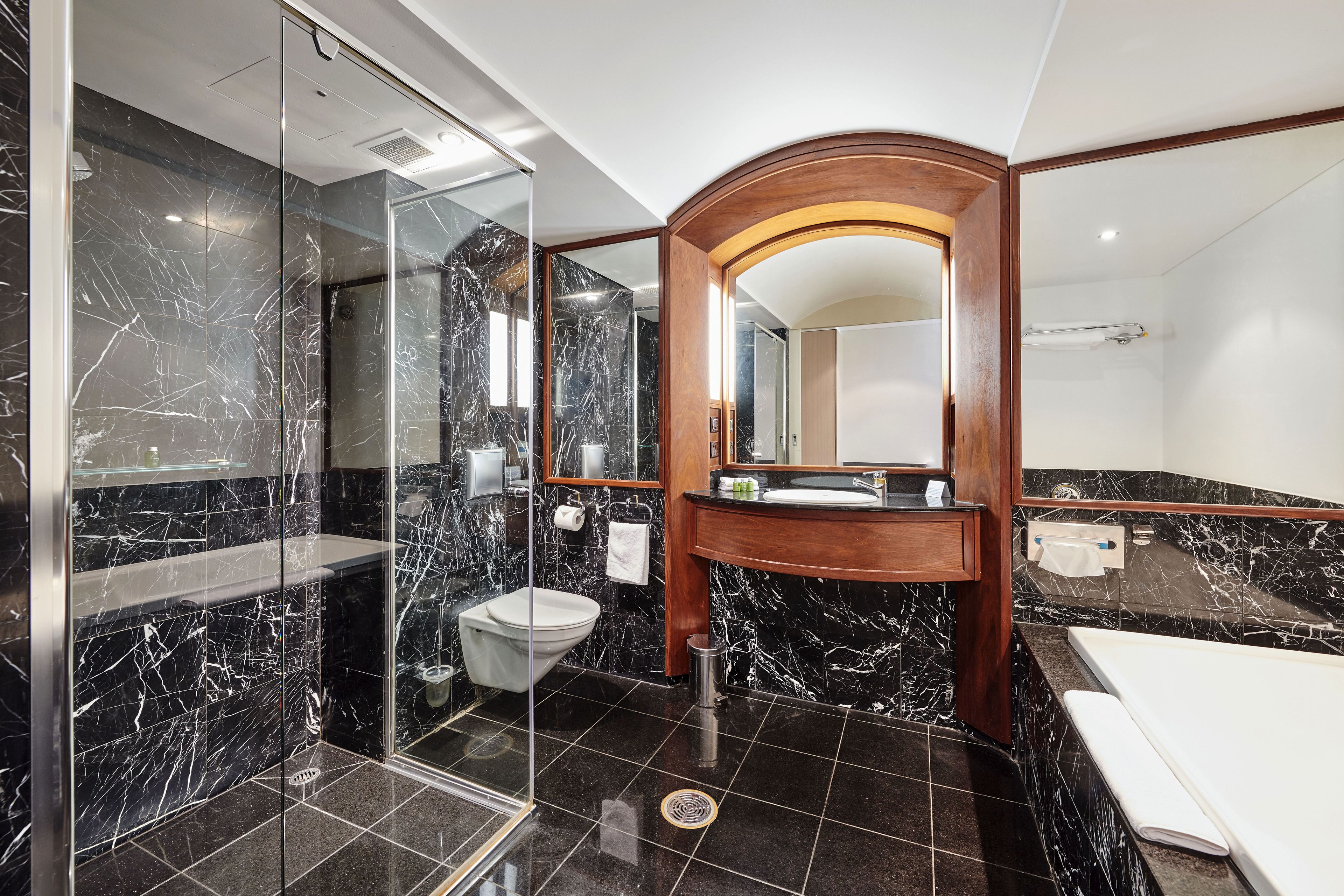 Een moderne badkamer met een douchecabine van glas, een houten wastafelmeubel, een wit toilet en een bad.