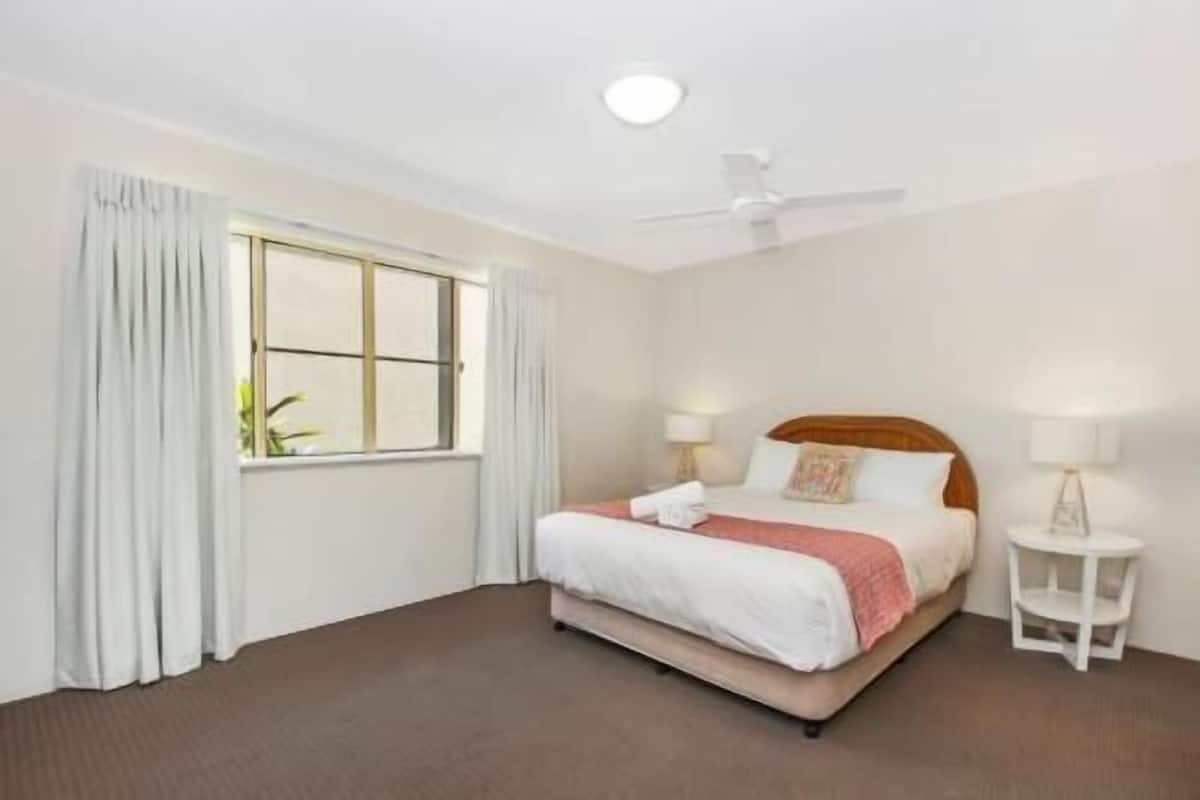 Ein Hotelzimmer mit einem Bett, einem Deckenventilator, einem Nachttisch mit Lampe und einem Fenster mit Vorhängen.