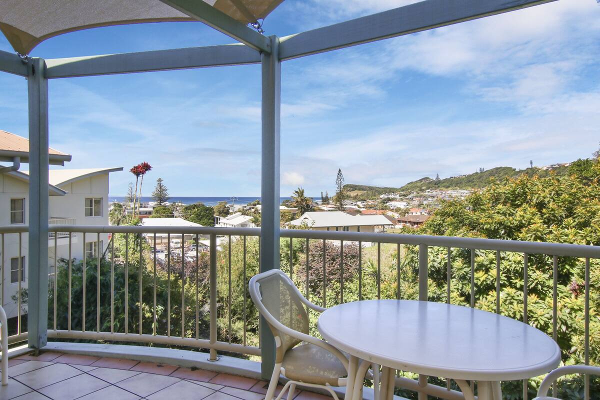 Ein Balkon mit Tisch und Stühlen, der auf einen Wohnbereich mit Häusern und Grünflächen blickt.