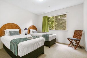 Una habitación con dos camas, una silla y un ventanal con cortinas.