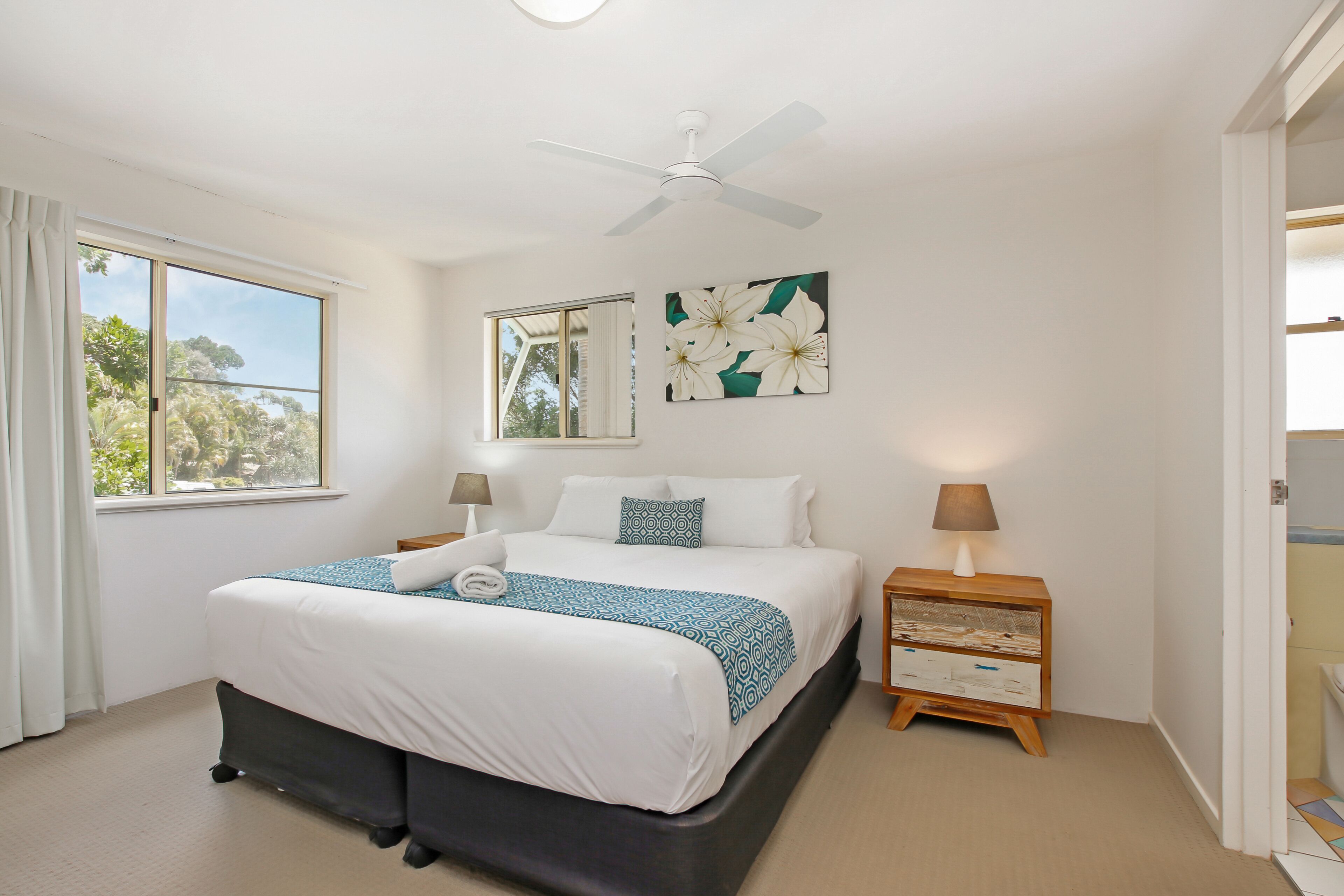 A bedroom with a bed, a ceiling fan, a window, a nightstand, and a wall-mounted mirror.