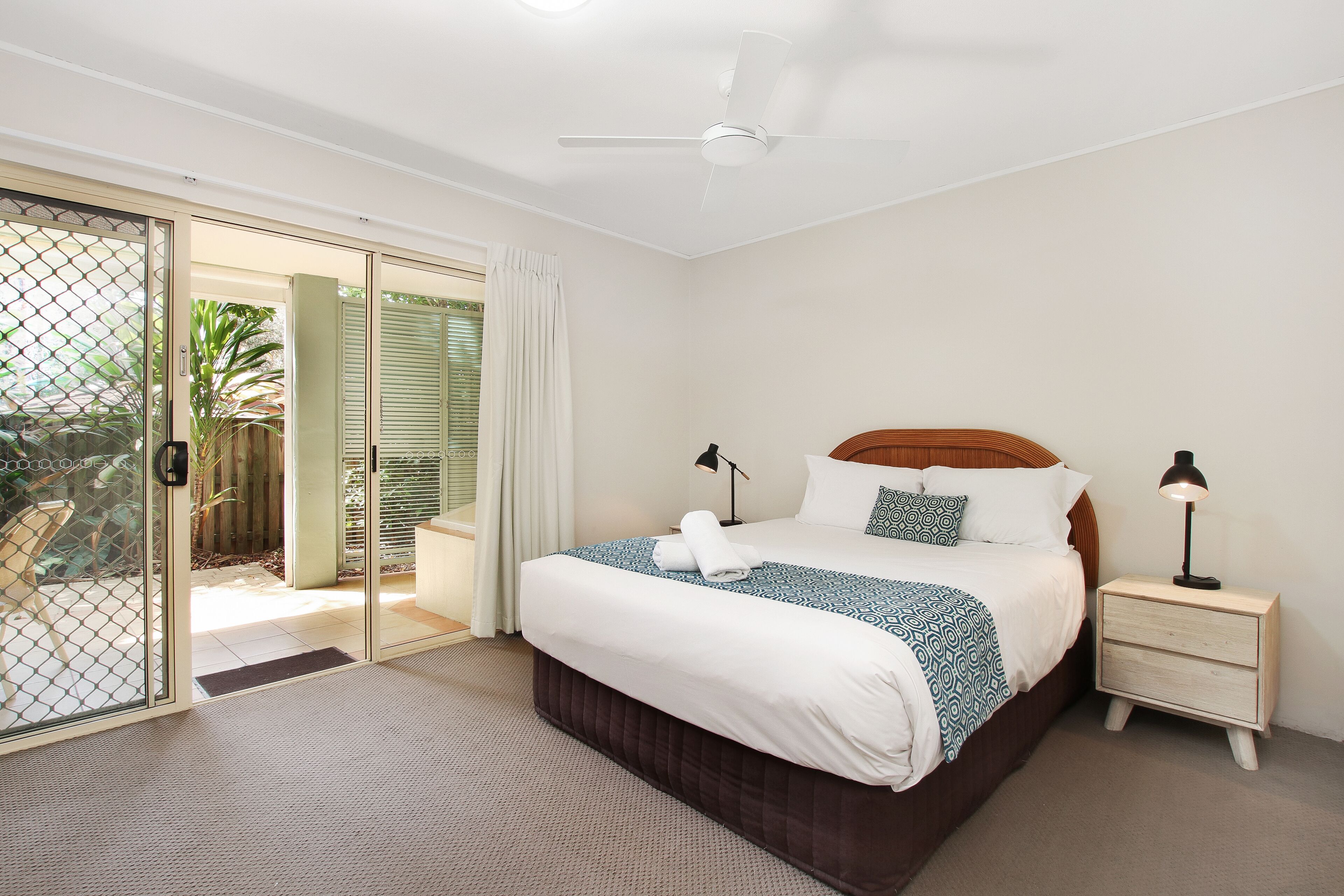 A bedroom with a bed, nightstands, a ceiling fan, and a sliding glass door leading to an outdoor area.