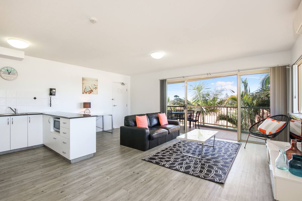 Eine moderne Wohnung mit Küche, Wohnbereich und Balkon mit Blick auf Palmen.