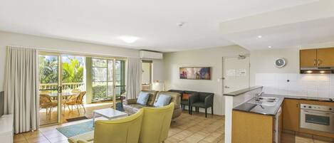 A spacious living area with a dining table, yellow chairs, a sofa, and a kitchen with a sink and stove.
