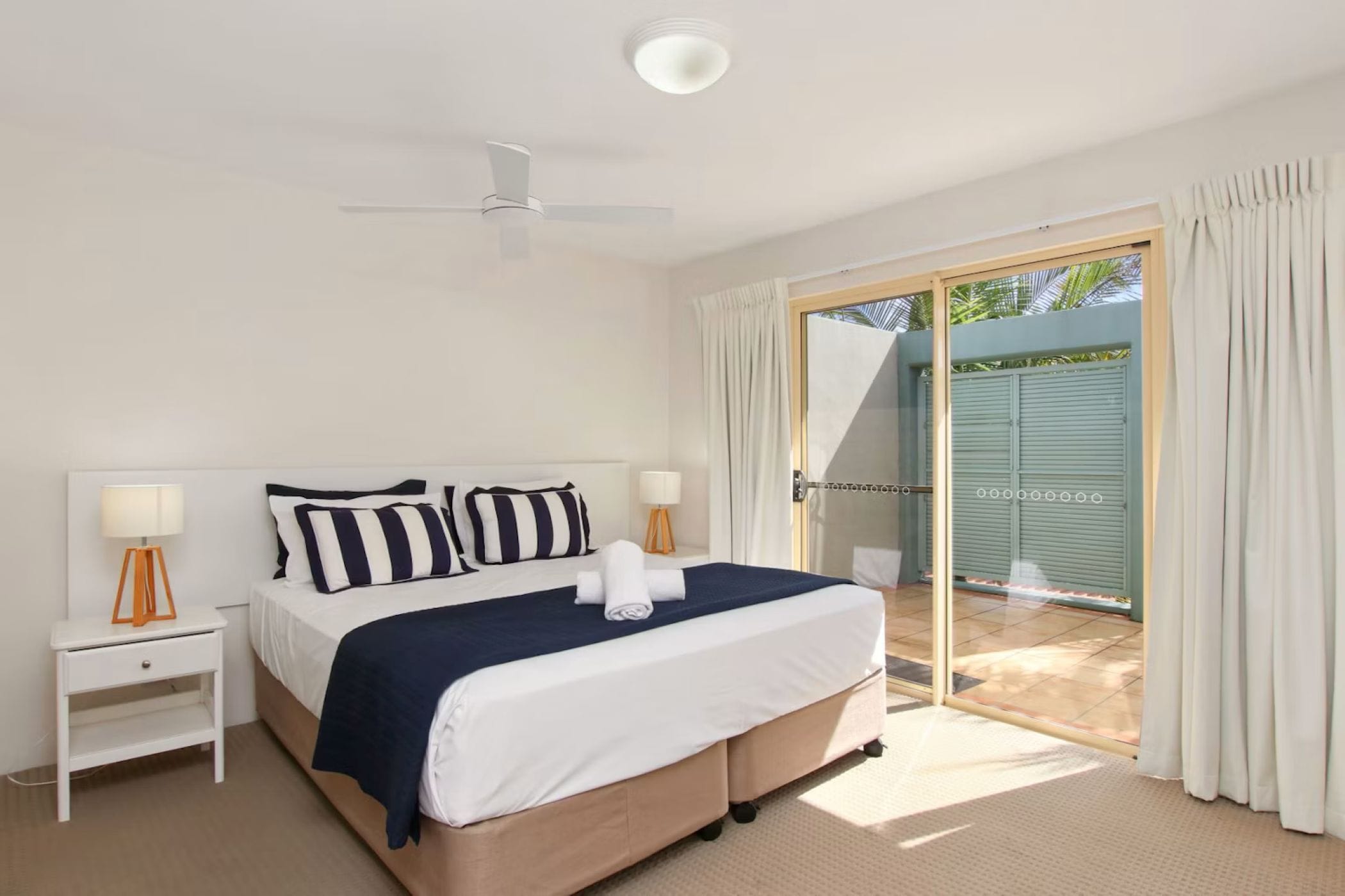 A bedroom with a bed, nightstands, a ceiling fan, and a sliding glass door leading to an outdoor area.