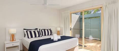 A bedroom with a bed, nightstands, a ceiling fan, and a sliding glass door leading to an outdoor area.