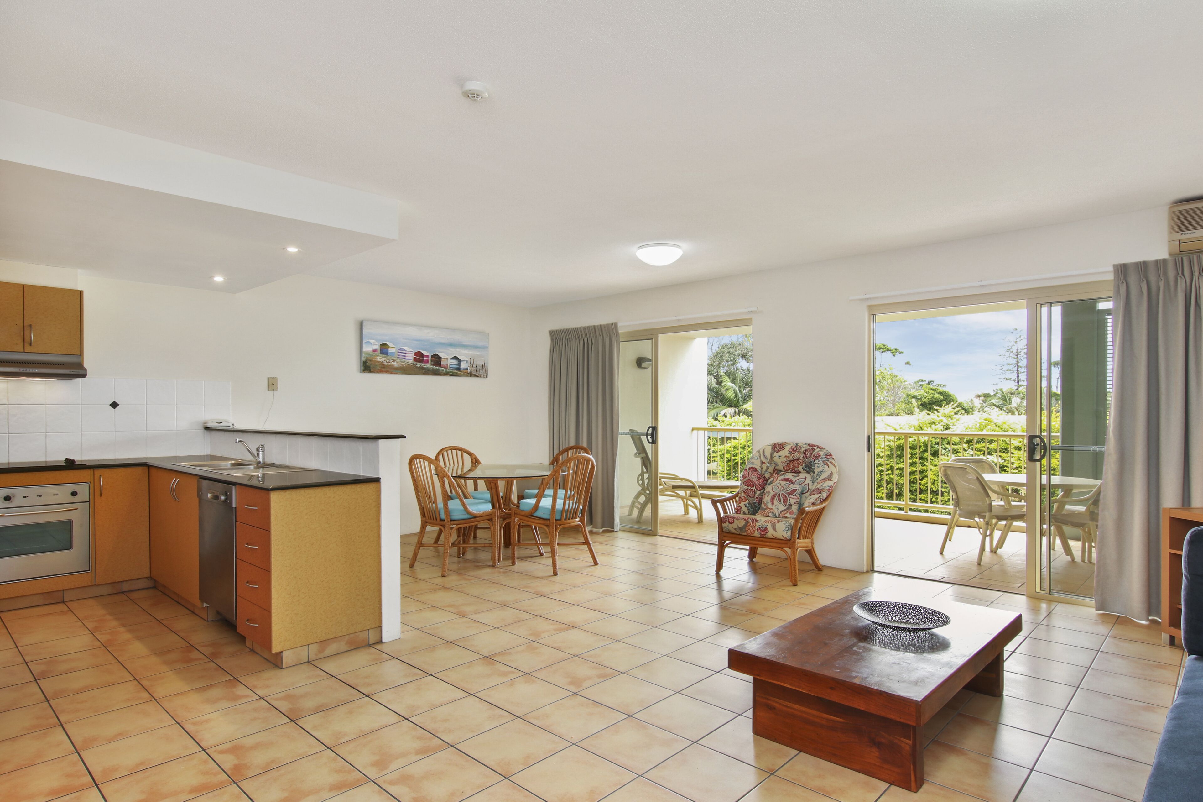 A modern kitchen with a dining area, a wooden table, and a balcony with outdoor seating.