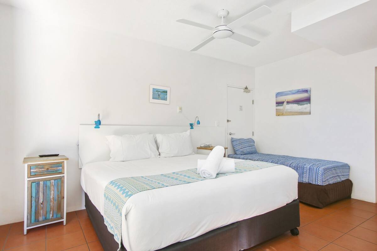 Ein Schlafzimmer mit Bett, Nachttisch, Deckenventilator und einer Wandlampe.