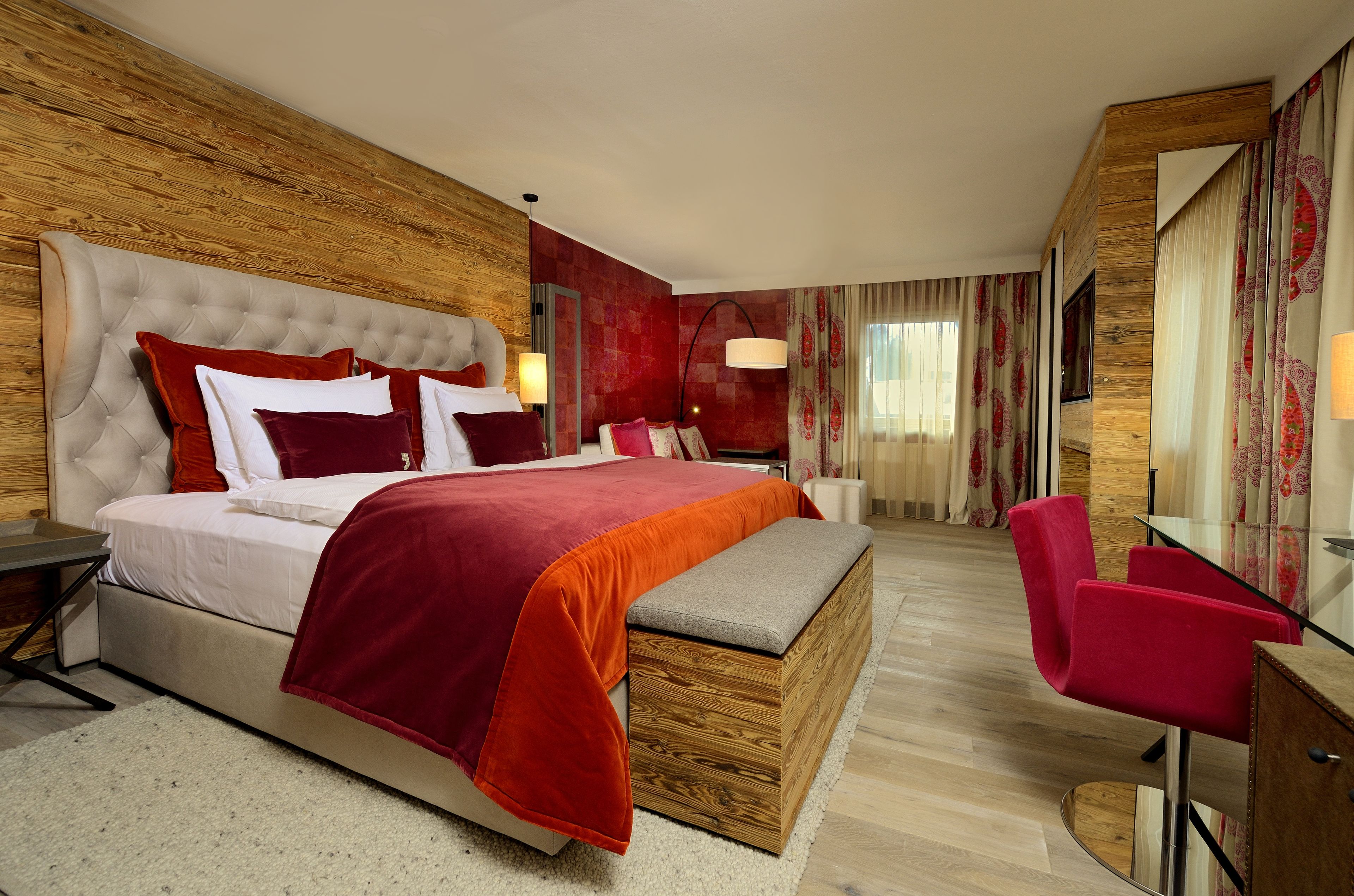 Una habitación de hotel con una cama grande, cabecera de madera, una banca, un escritorio y una silla.