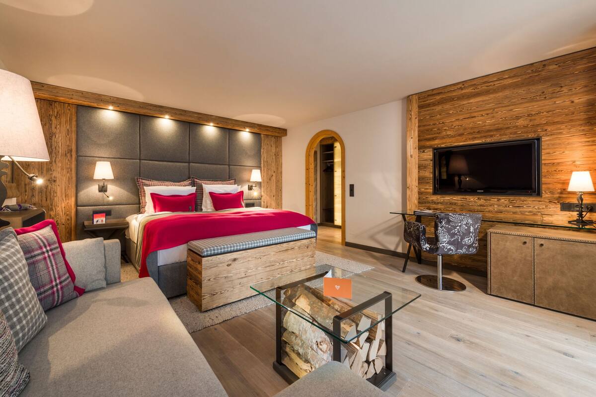 A modern hotel room with a large bed, a sofa, a TV, and a wooden accent wall.