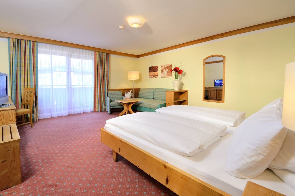 A hotel room with a wooden bed, a desk with a computer, a chair, a small table, and a lamp.