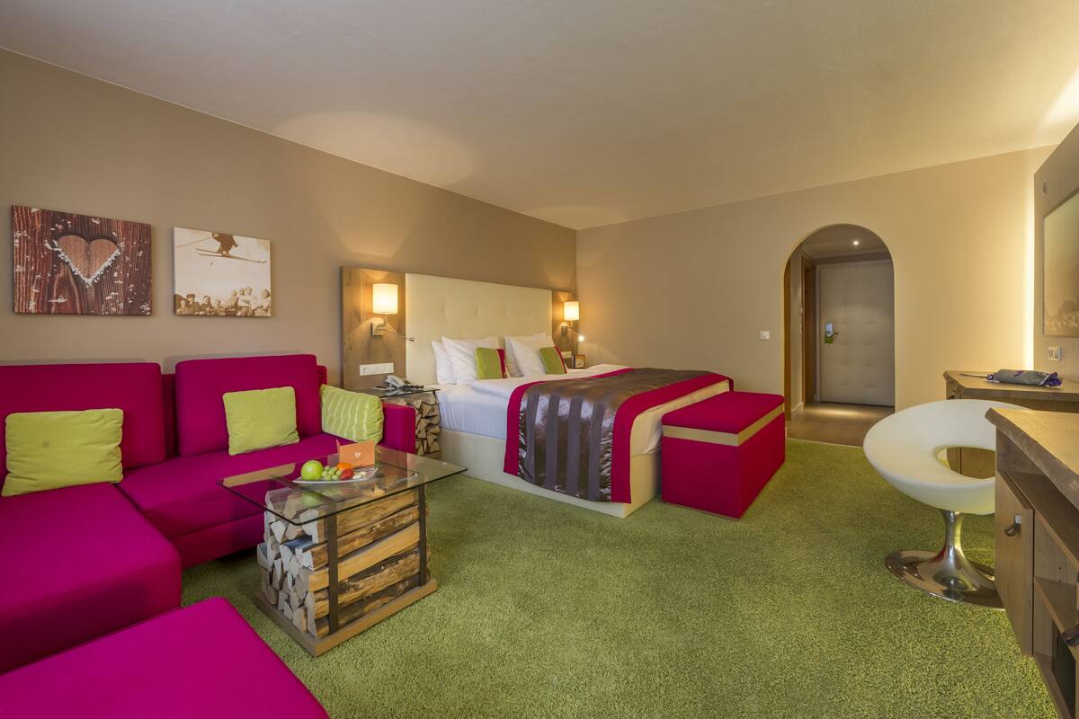 A hotel room with a bed, a red sofa, a glass coffee table, and a small bathroom.