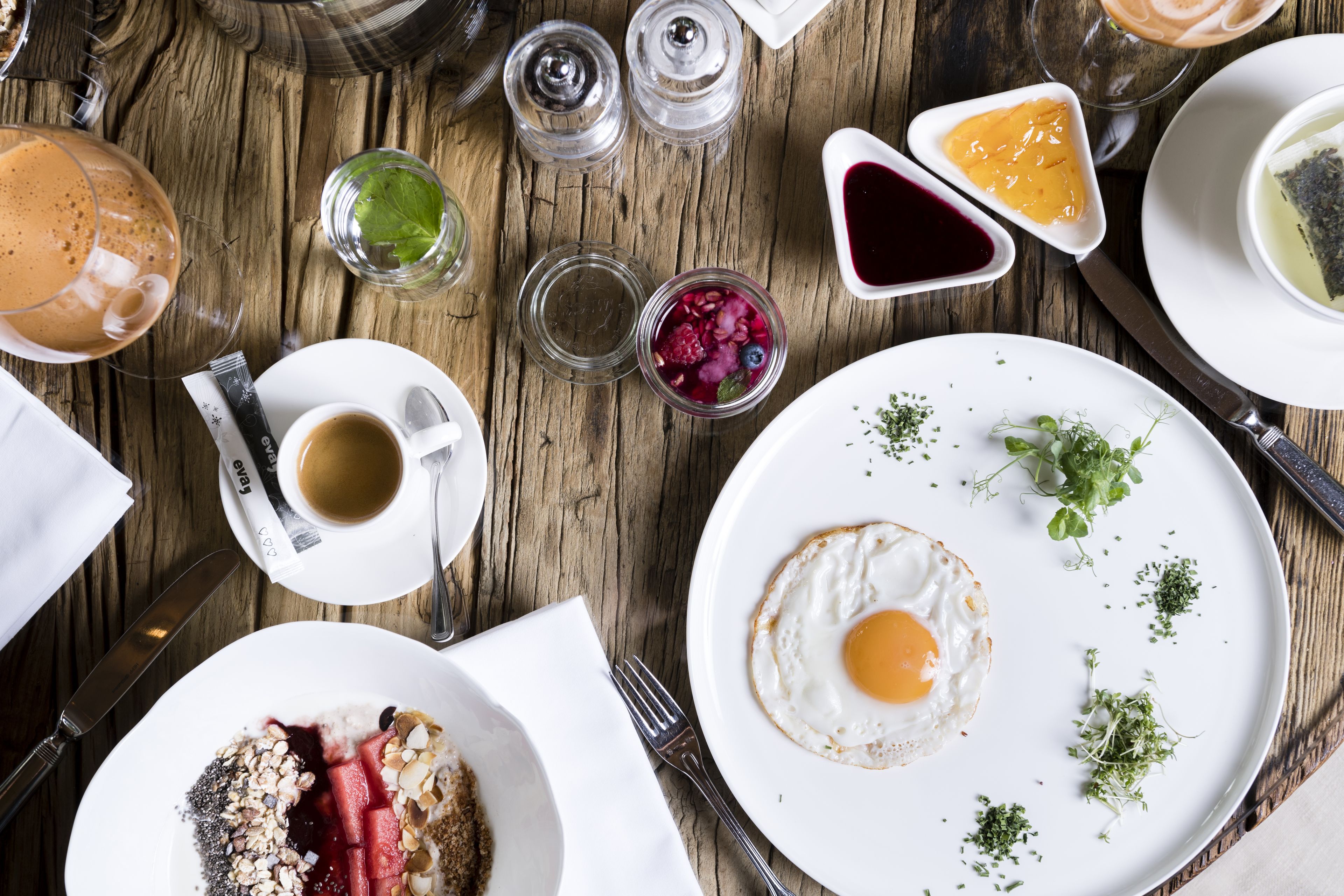A wooden table with various breakfast items including a plate with a fried egg, a cup of coffee, and several small dishes with condiments.
