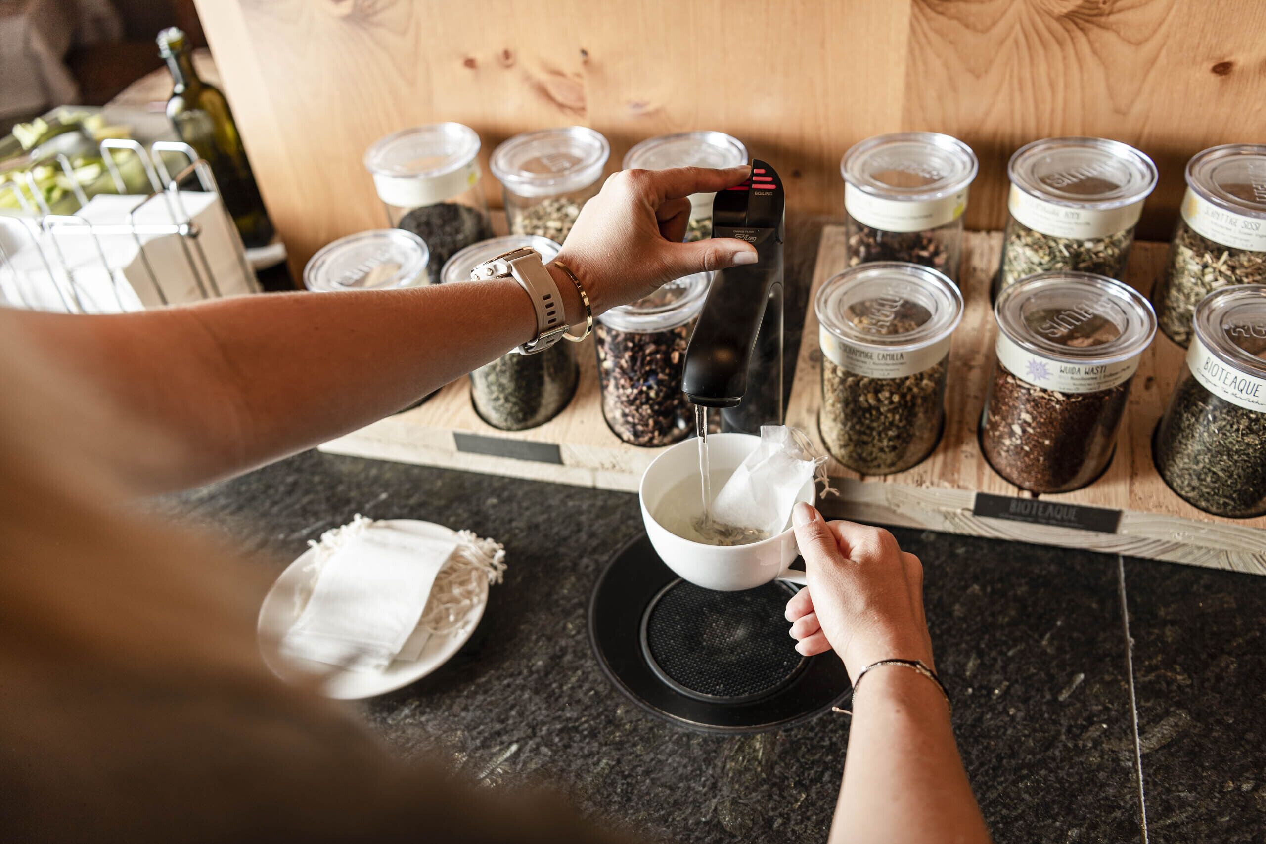A person using a coffee machine to brew coffee, with jars of coffee beans in the background.