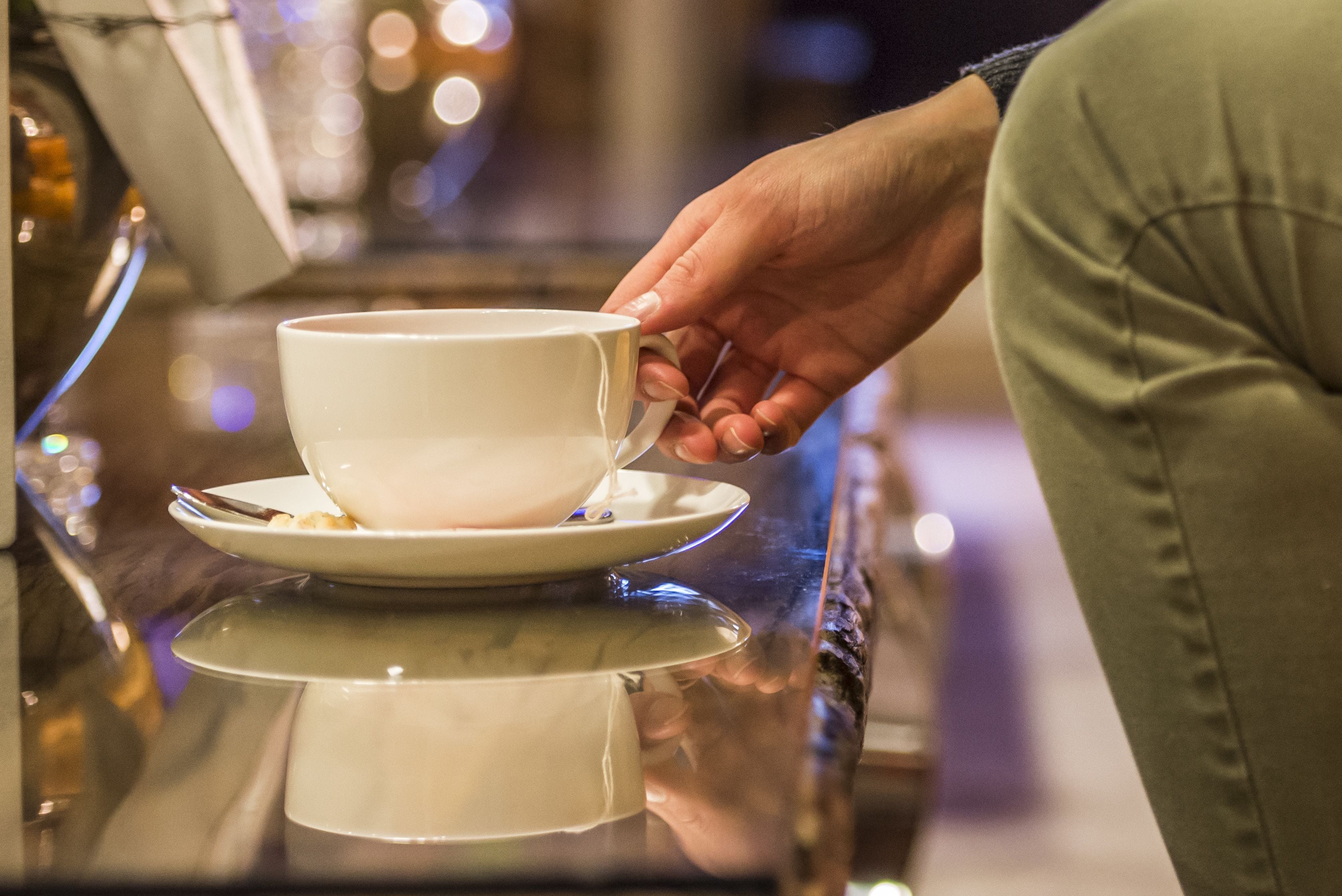 A hand holding a white cup on a reflective surface.