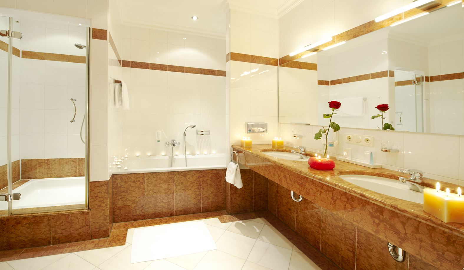 A modern bathroom with a bathtub, a shower, and a vanity with a sink and mirror. There are candles on the vanity and a red rose in a vase.