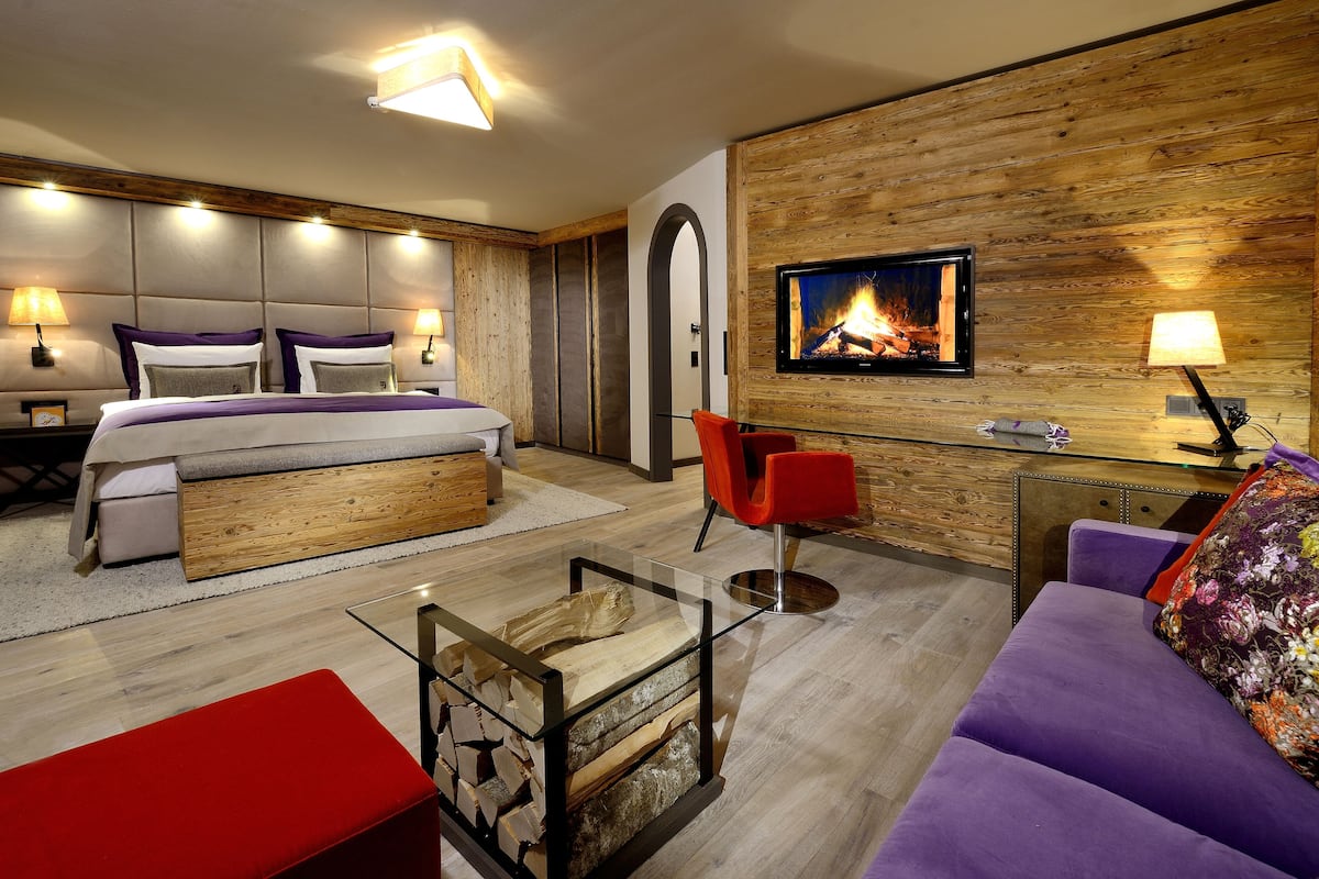 A modern hotel room with a bed, a desk, a sofa, and a fireplace.