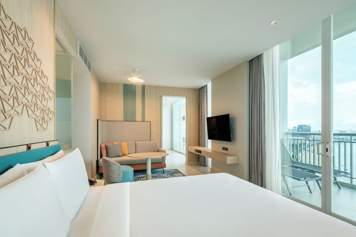 Une chambre d’hôtel avec un grand lit, un canapé, une télévision et un balcon offrant une vue sur la ville.