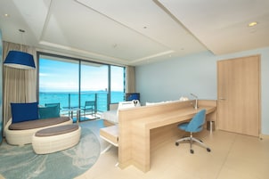Una habitación de hotel moderna con un balcón amplio, un escritorio de madera, un rincón de estar cómodo y vistas al mar.