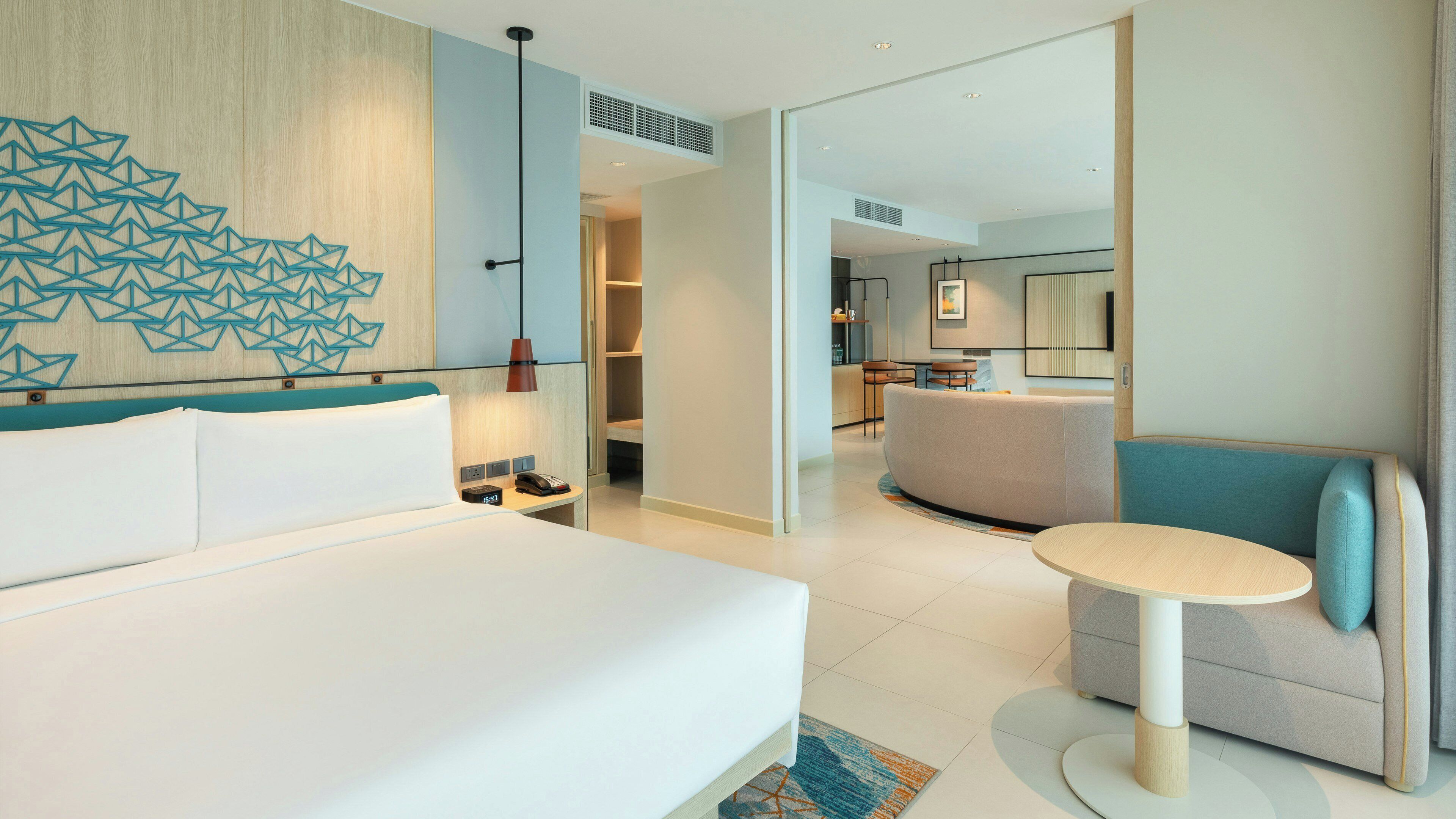 A modern hotel room with a large bed, a seating area, and a view into the dining area.