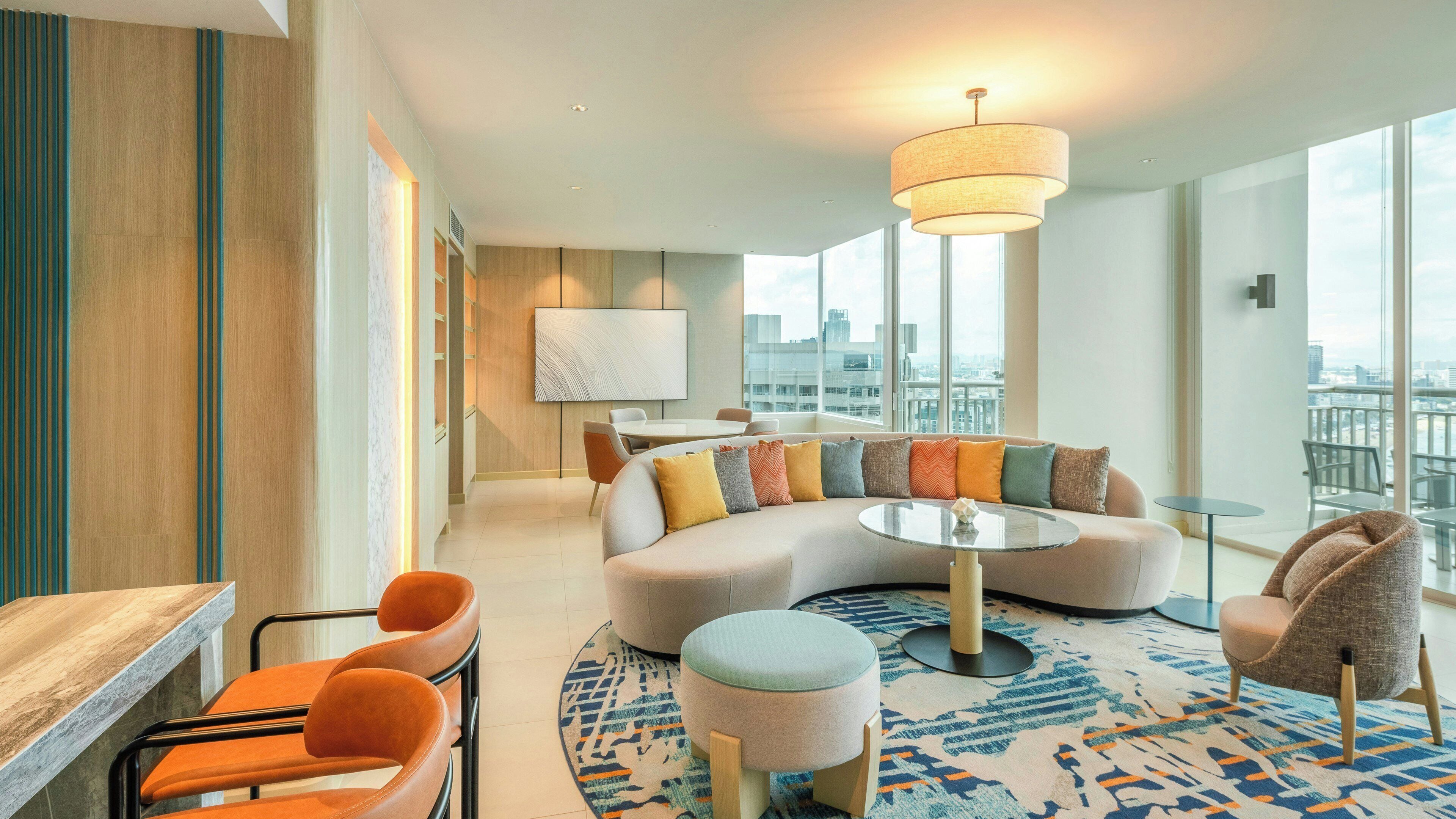 A modern living room with a sofa, ottoman, and chairs, a round coffee table, and a large window with a city view.