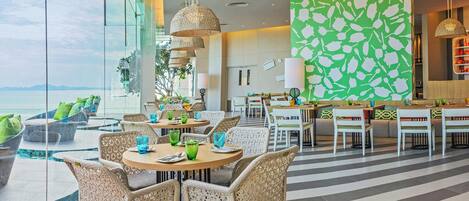 A modern dining area with wicker chairs, round tables, and a view of the sea.