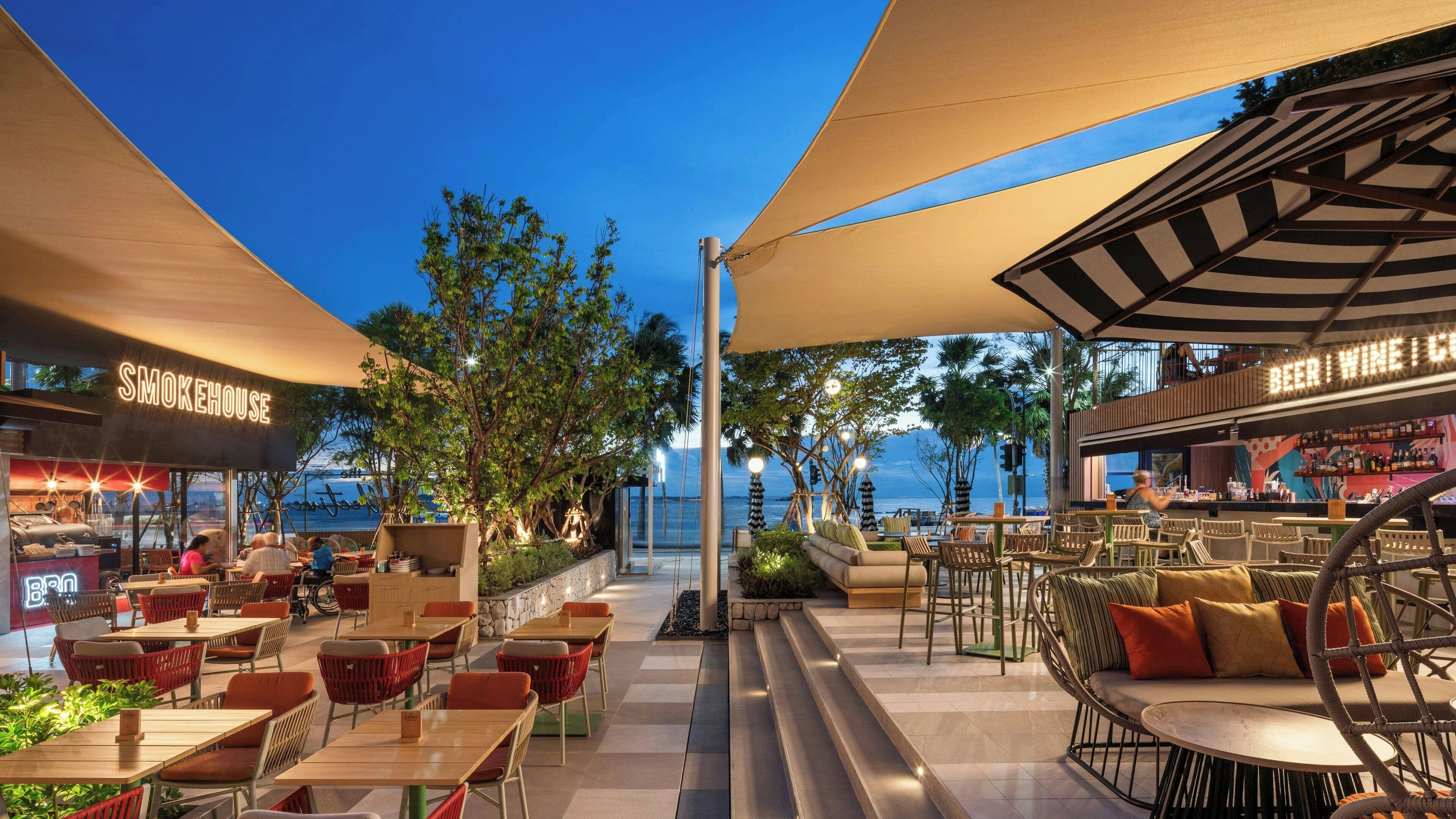 An outdoor dining area with tables and chairs, a bar, and a view of the ocean.
