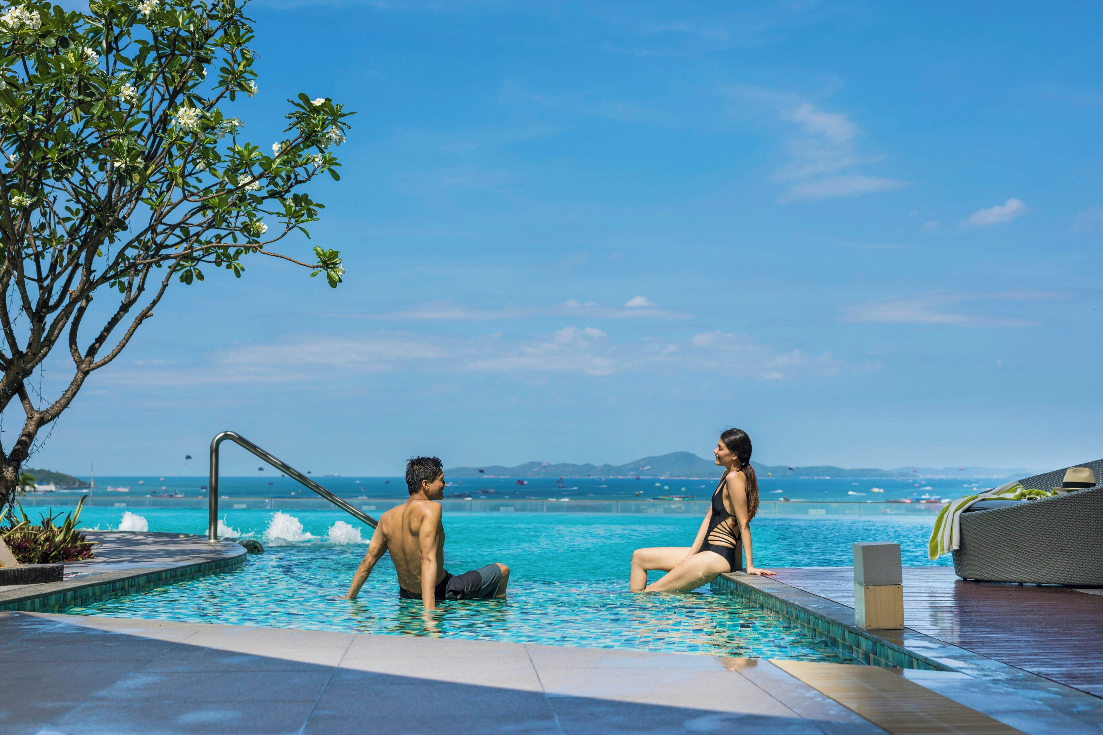 A pool area with a view of the sea, a tree, and a couple.