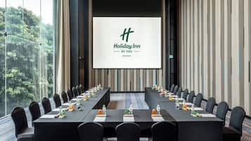 Un salón de conferencias con una larga mesa, sillas y una pantalla que muestra el logotipo de Holiday Inn.