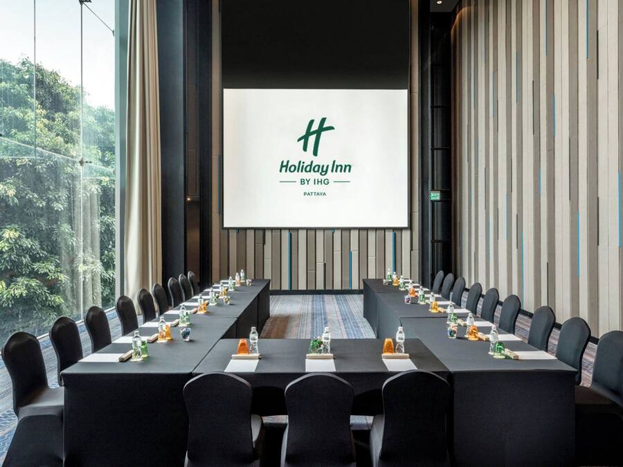 Un salón de conferencias con una larga mesa, sillas y una pantalla que muestra el logotipo de Holiday Inn.