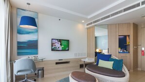 Una habitación de hotel moderna con escritorio, silla de oficina, sofá y un televisor mostrando un menú.