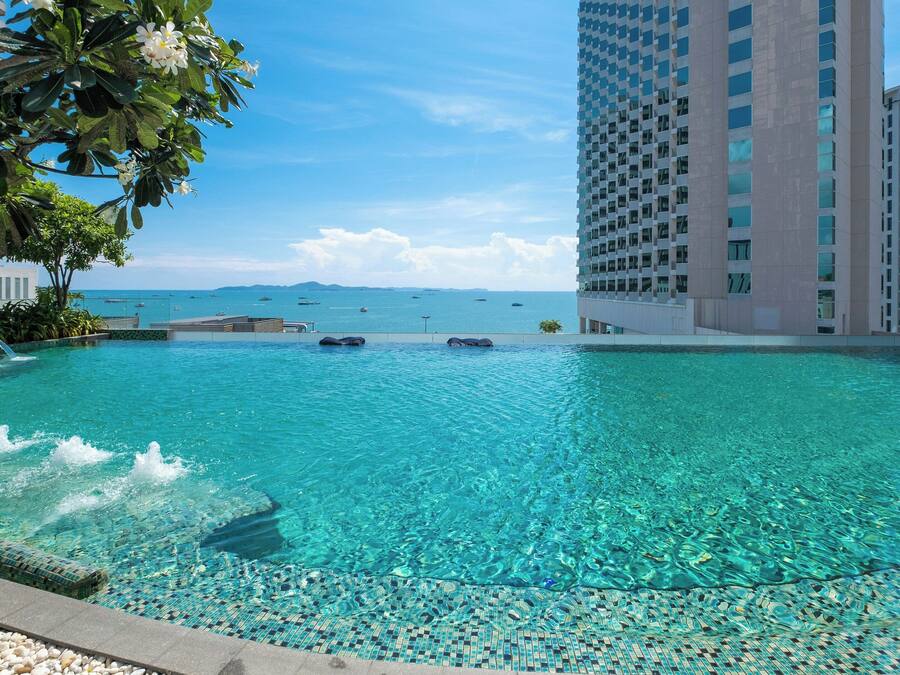 Una piscina azul cristalina con borde de azulejos, rodeada por un edificio alto y vista al mar.
