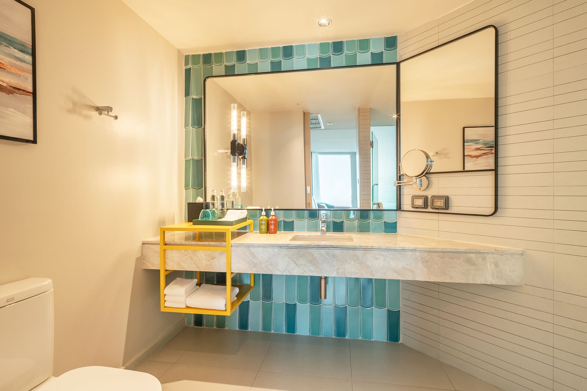 A bathroom with a large mirror, a marble sink, and a yellow towel rack.