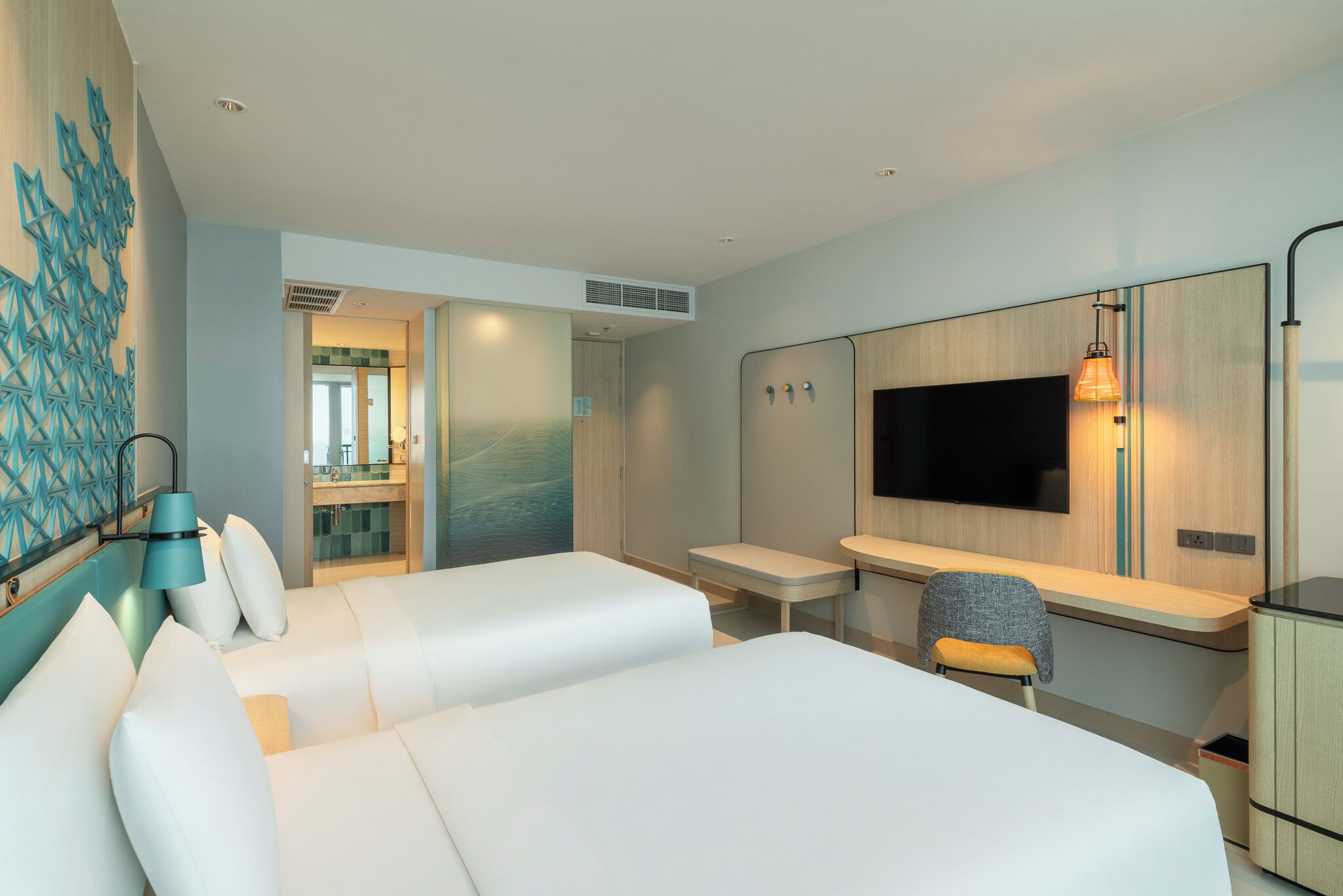 A hotel room with two beds, a desk, a TV, and a bathroom visible through an open door.
