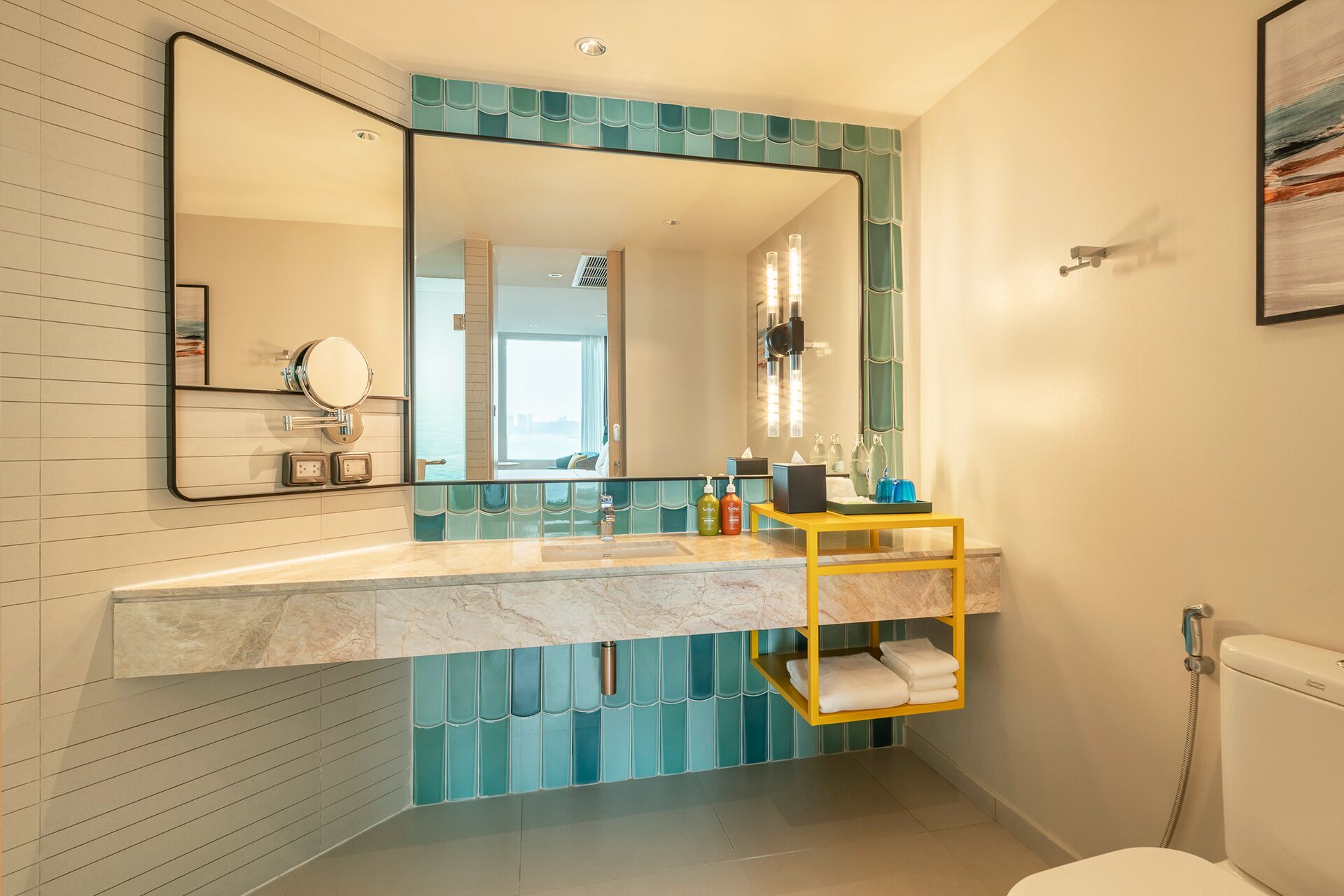 A modern bathroom with a large mirror, a marble countertop, and a yellow towel rack.