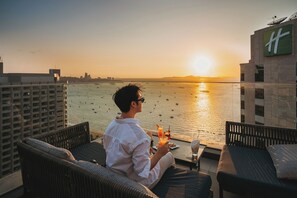A person seated on a balcony with a view of the sea and a sunset. - Holiday Inn Pattaya by IHG (Pattaya)