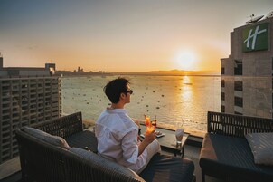Una persona sentada en un balcón con vista al mar y al atardecer.