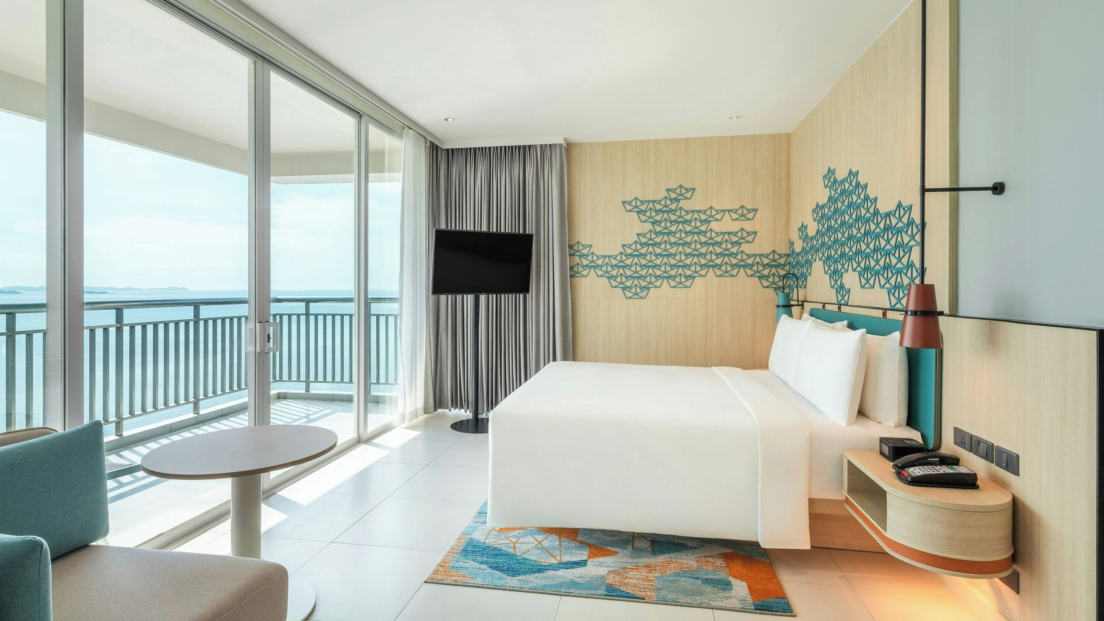 Habitación de hotel con cama, televisión, escritorio, silla y vista al mar.