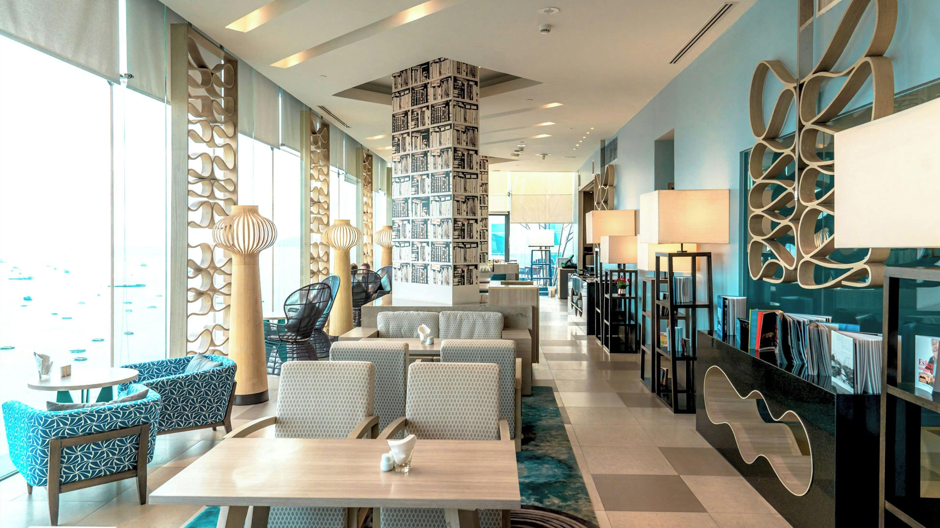 A modern hotel lobby with seating areas, a central bookshelf, and decorative wall panels.