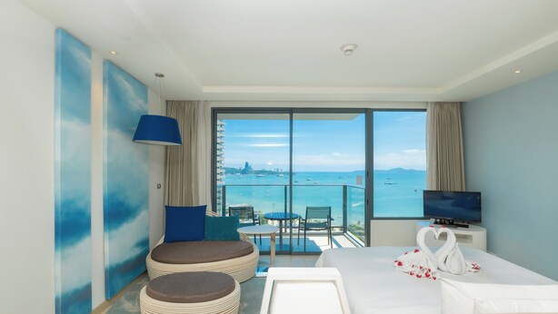 A hotel room with a balcony, a bed with a heart-shaped towel arrangement, a television, and a view of the sea and cityscape. - Holiday Inn Pattaya by IHG (Pattaya)