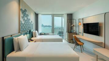 A hotel room with two beds, a desk, a TV, and a view of the city through large windows.