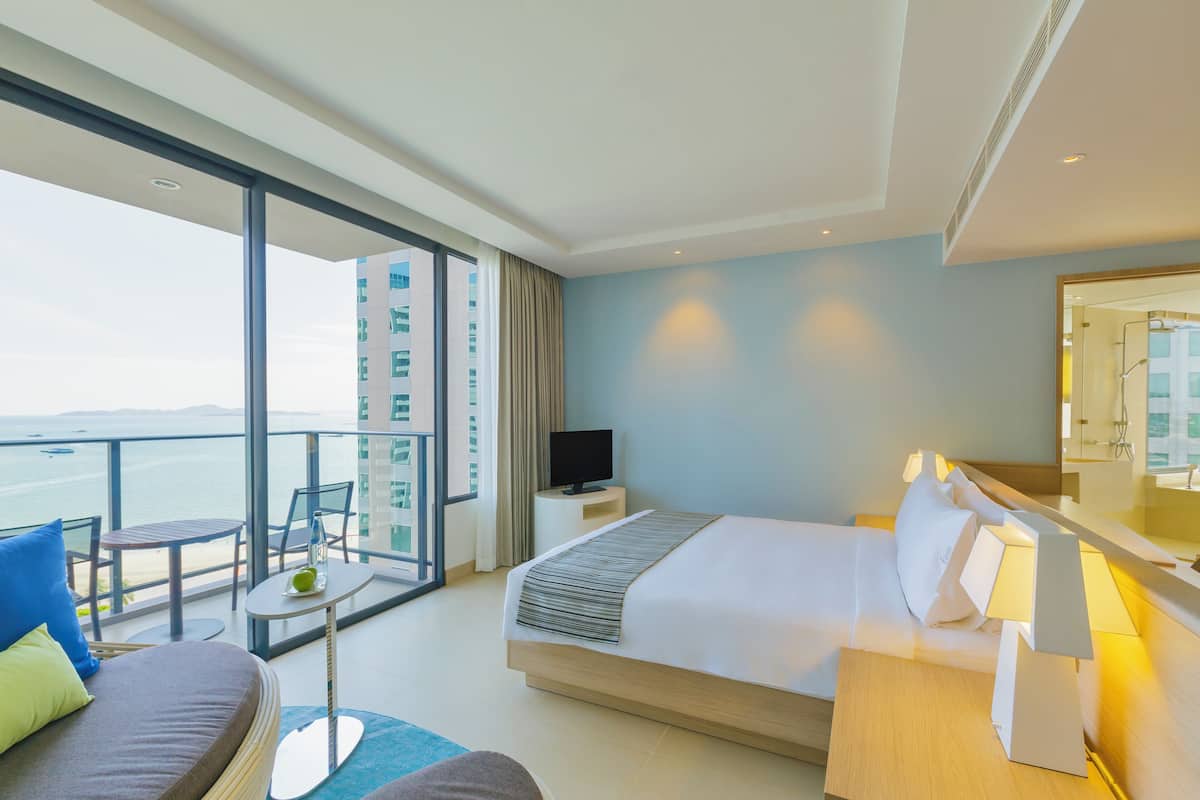 A hotel room with a balcony, a bed, a TV, and a desk with a lamp.