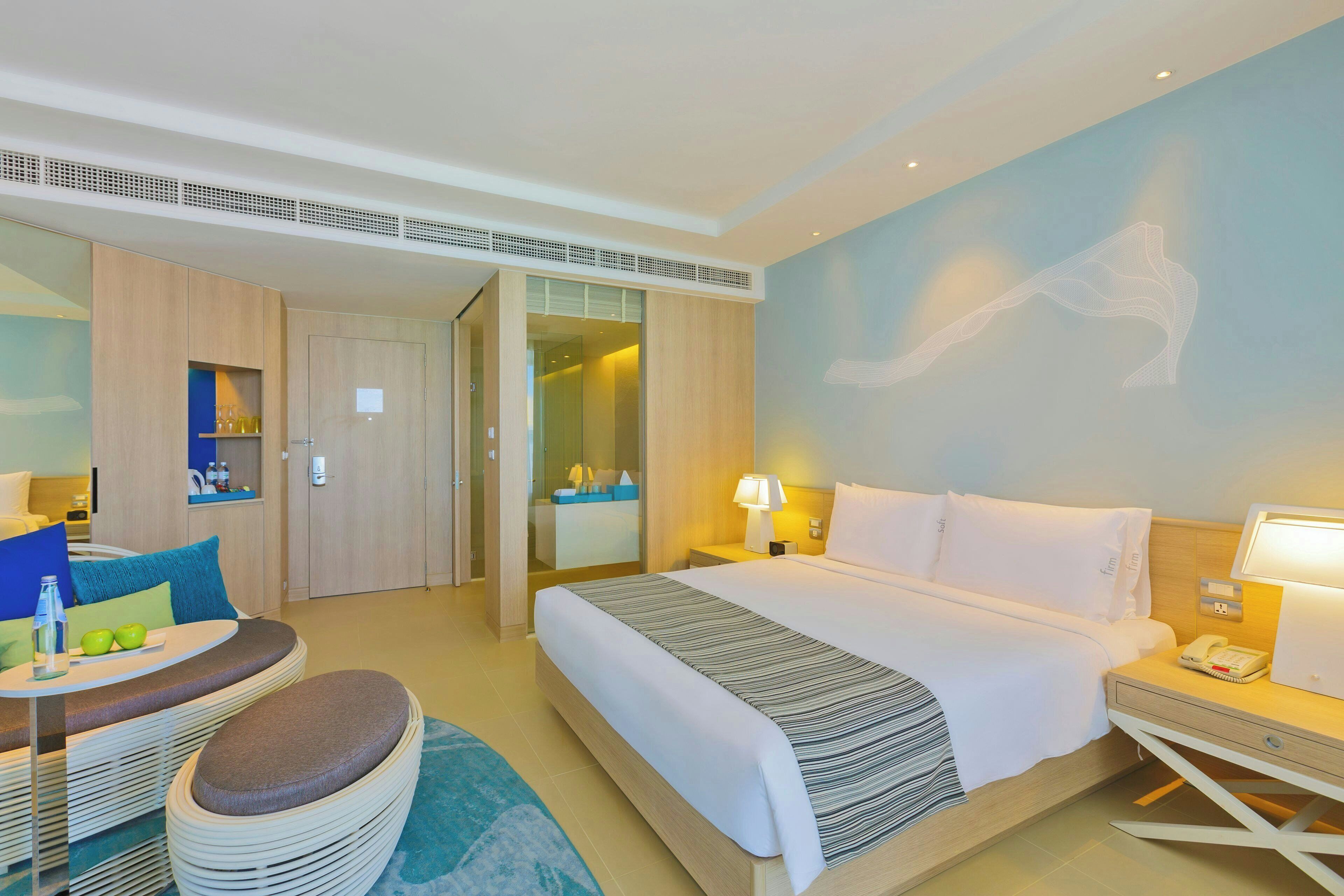 A hotel room with a bed, bedside table, lamp, and a desk with a chair.