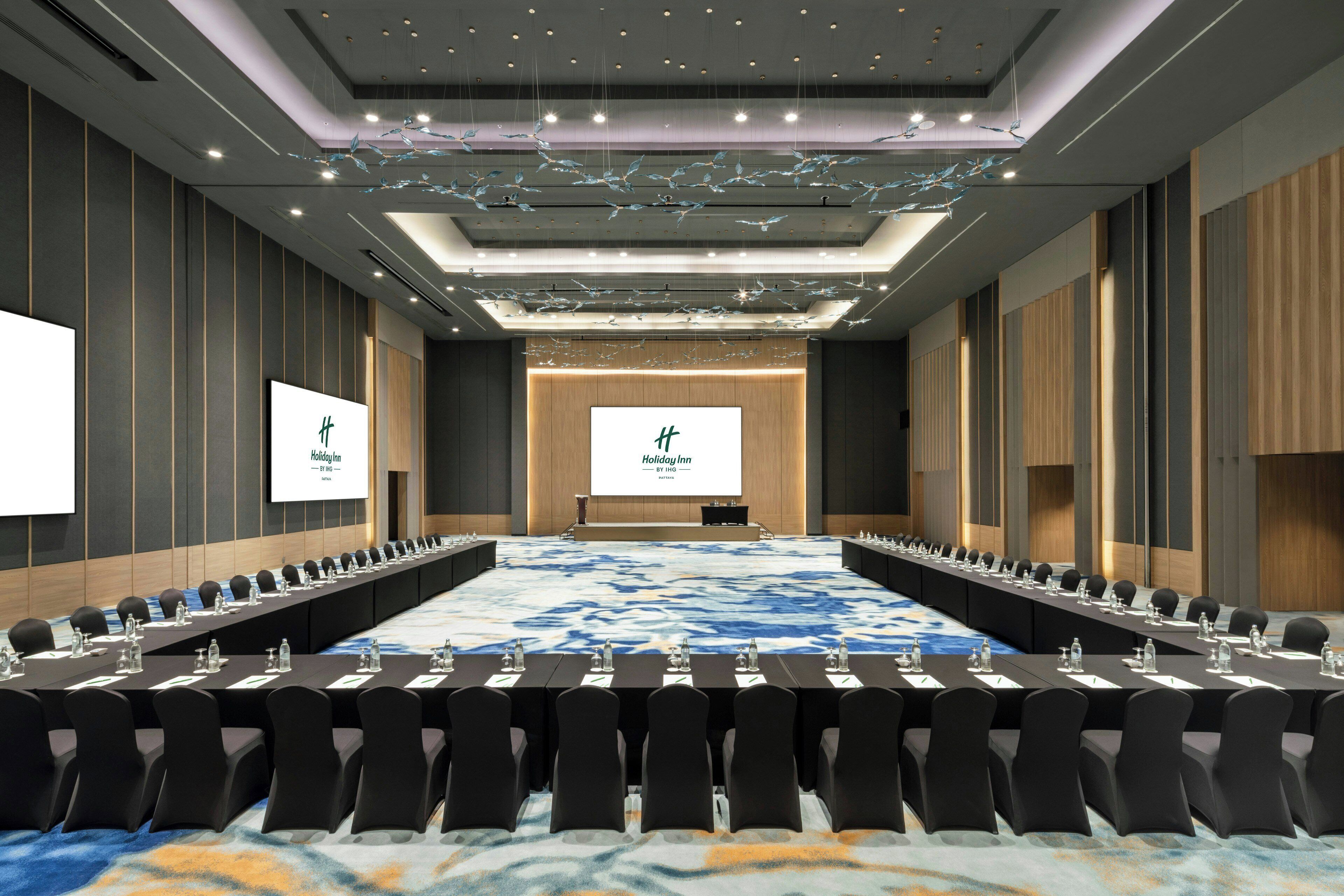A conference room with a long table, rows of chairs, and two screens displaying the Holiday Inn logo.
